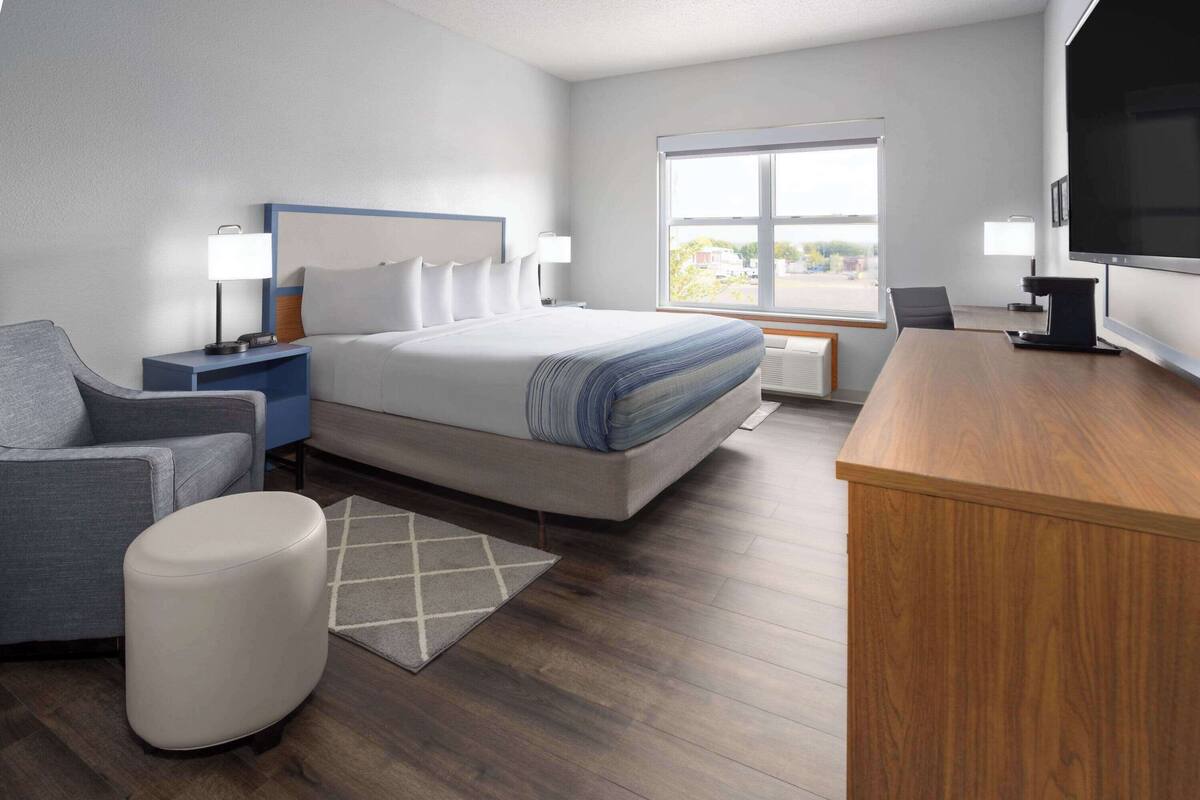 A modern hotel room with a large bed, a desk, a chair, and a TV.