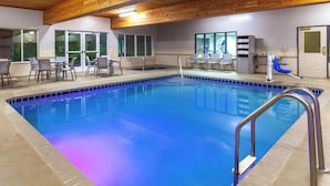 An indoor swimming pool with a tiled edge, a metal ladder, and a seating area with chairs and tables.