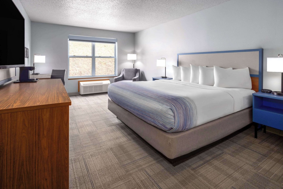 A hotel room with a large bed, a desk, a chair, a television, and a window.