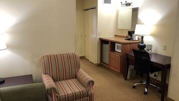 A compact hotel room with a striped armchair, a small desk with a chair, a microwave, and a coffee maker.