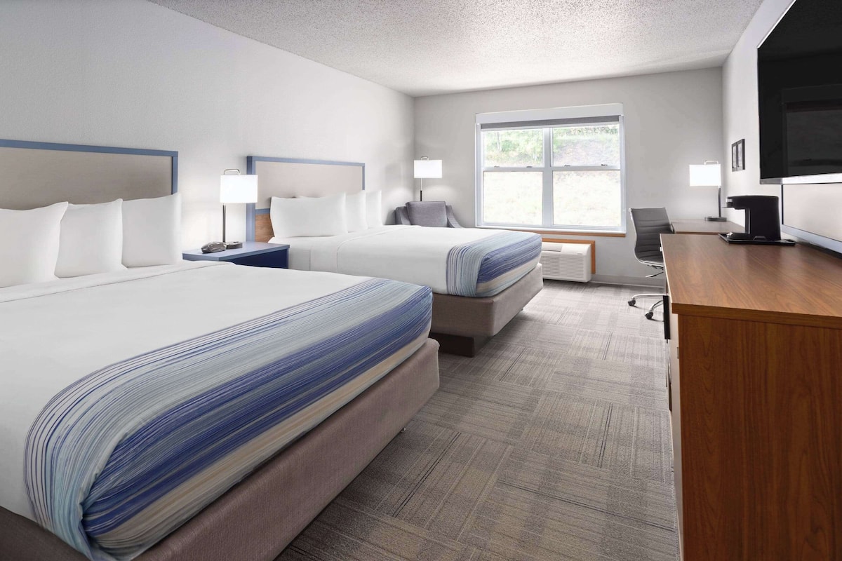A hotel room with two beds, a desk, a chair, a TV, and a window.