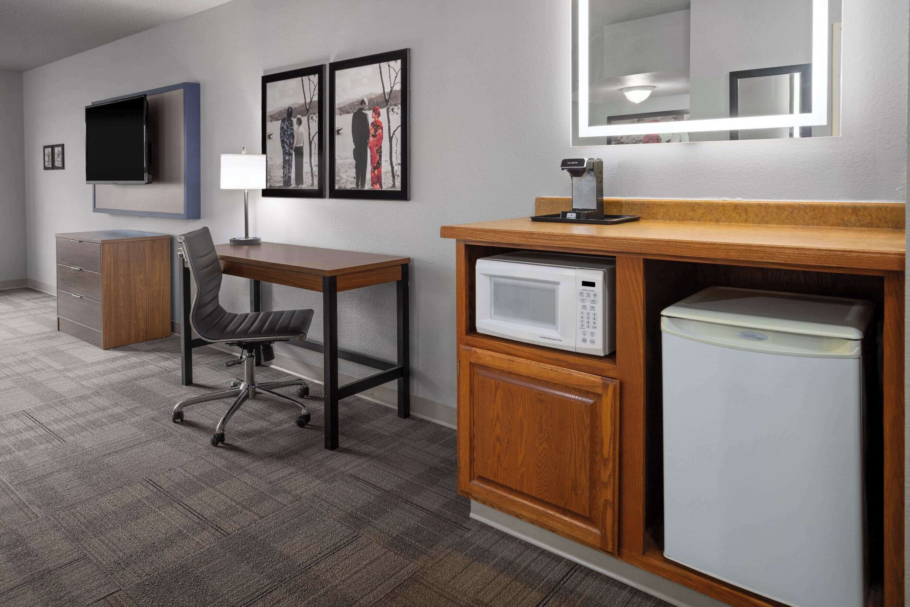 Habitación de hotel con escritorio, silla, televisor, microondas, refrigerador pequeño y armario de madera.