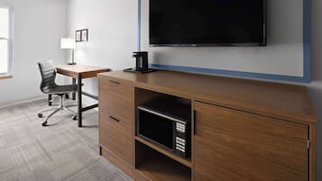 A modern office space with a wooden desk, a black office chair, a mounted flat-screen TV, a coffee machine, and a microwave.