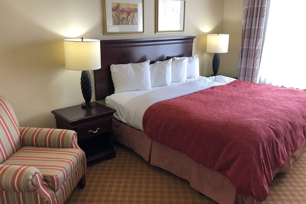 A hotel room with a large bed, two bedside lamps, a striped armchair, a nightstand, and two framed pictures on the wall.
