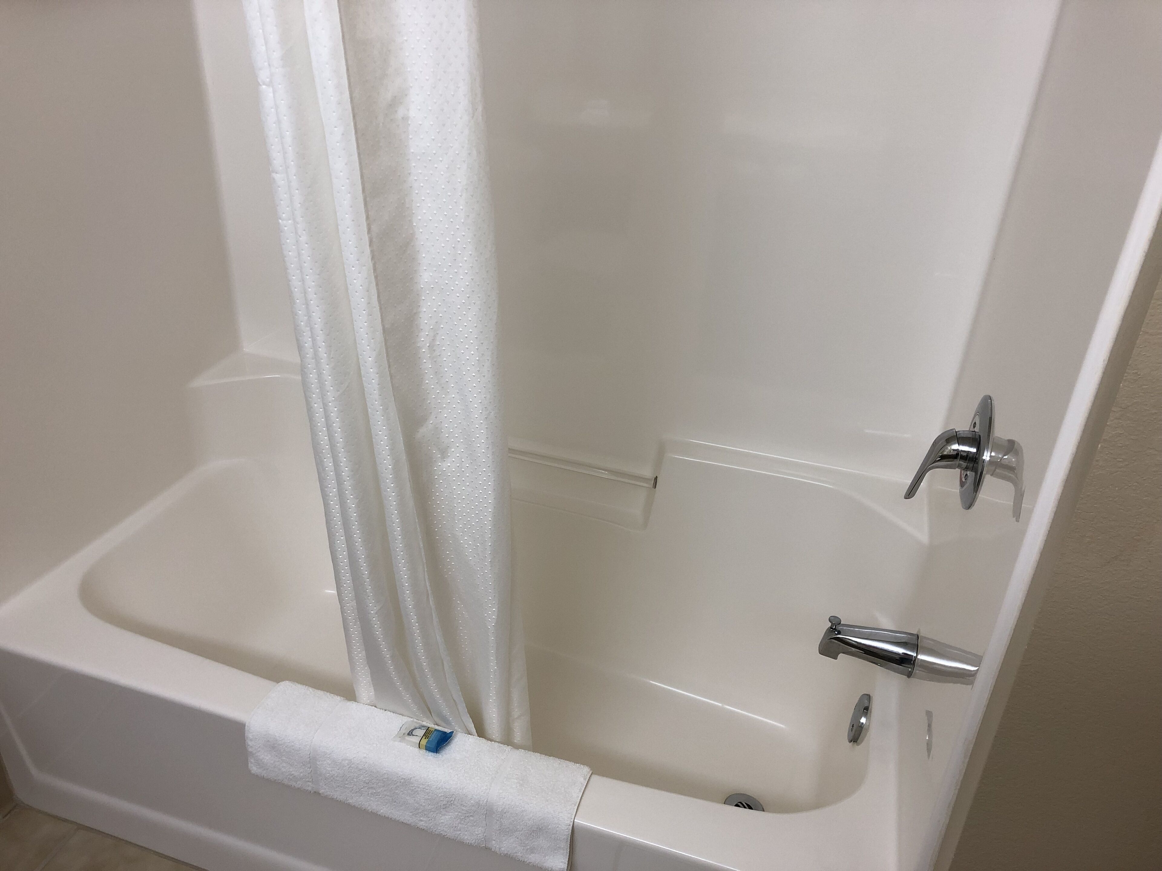 Una bañera blanca con cortina de ducha, una toalla y un grifo.