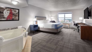A hotel room with a large bed, a separate desk, a bathtub, and a large window.