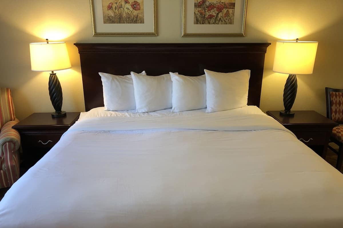 A neatly made bed with white linens, two bedside lamps, and two framed floral paintings on the wall.