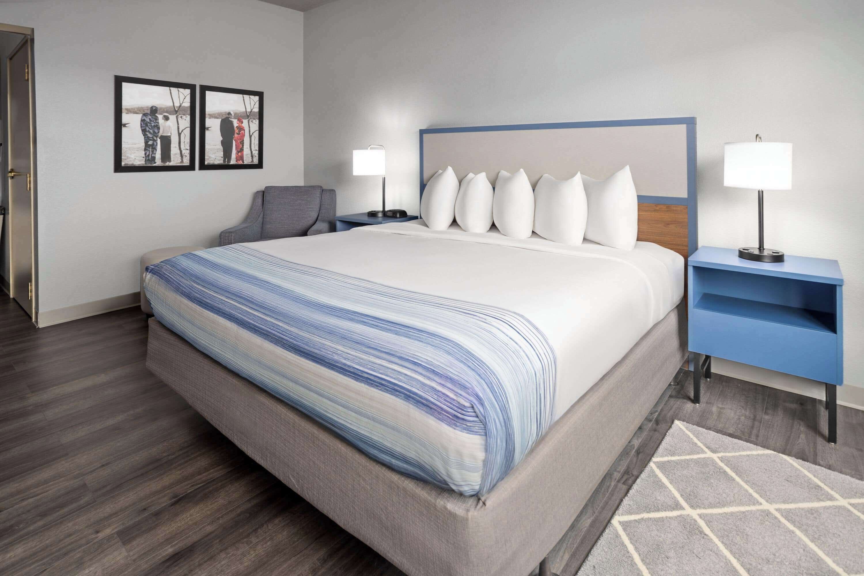 A hotel room with a large bed, two bedside tables with lamps, a gray armchair, and a rug.