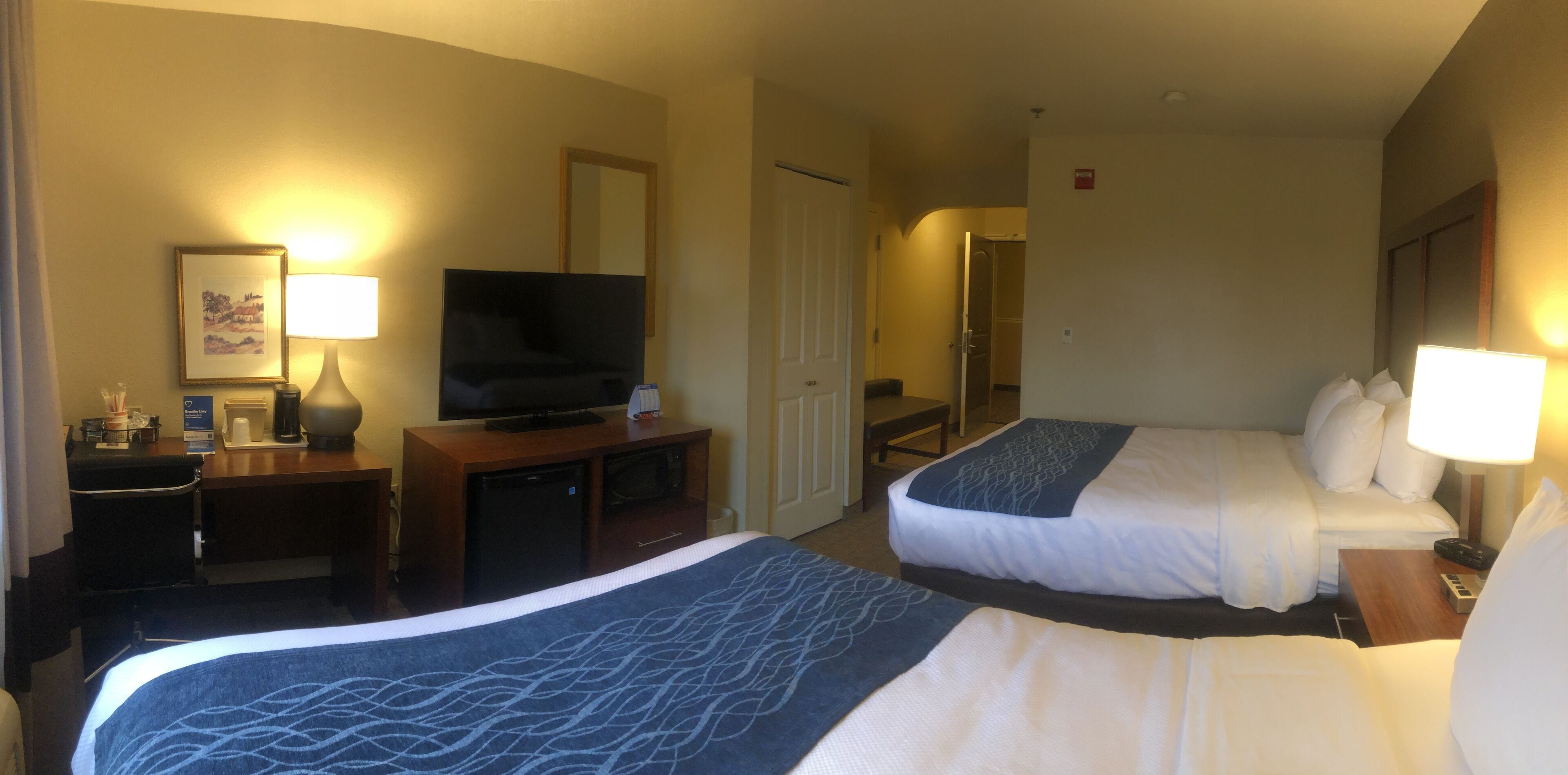 A hotel room with two beds, a television, a desk with a lamp, and a bathroom visible through an open door.