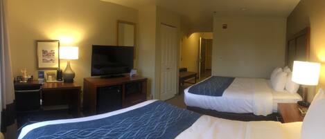 A hotel room with two beds, a television, a desk with a lamp, and a bathroom visible through an open door.