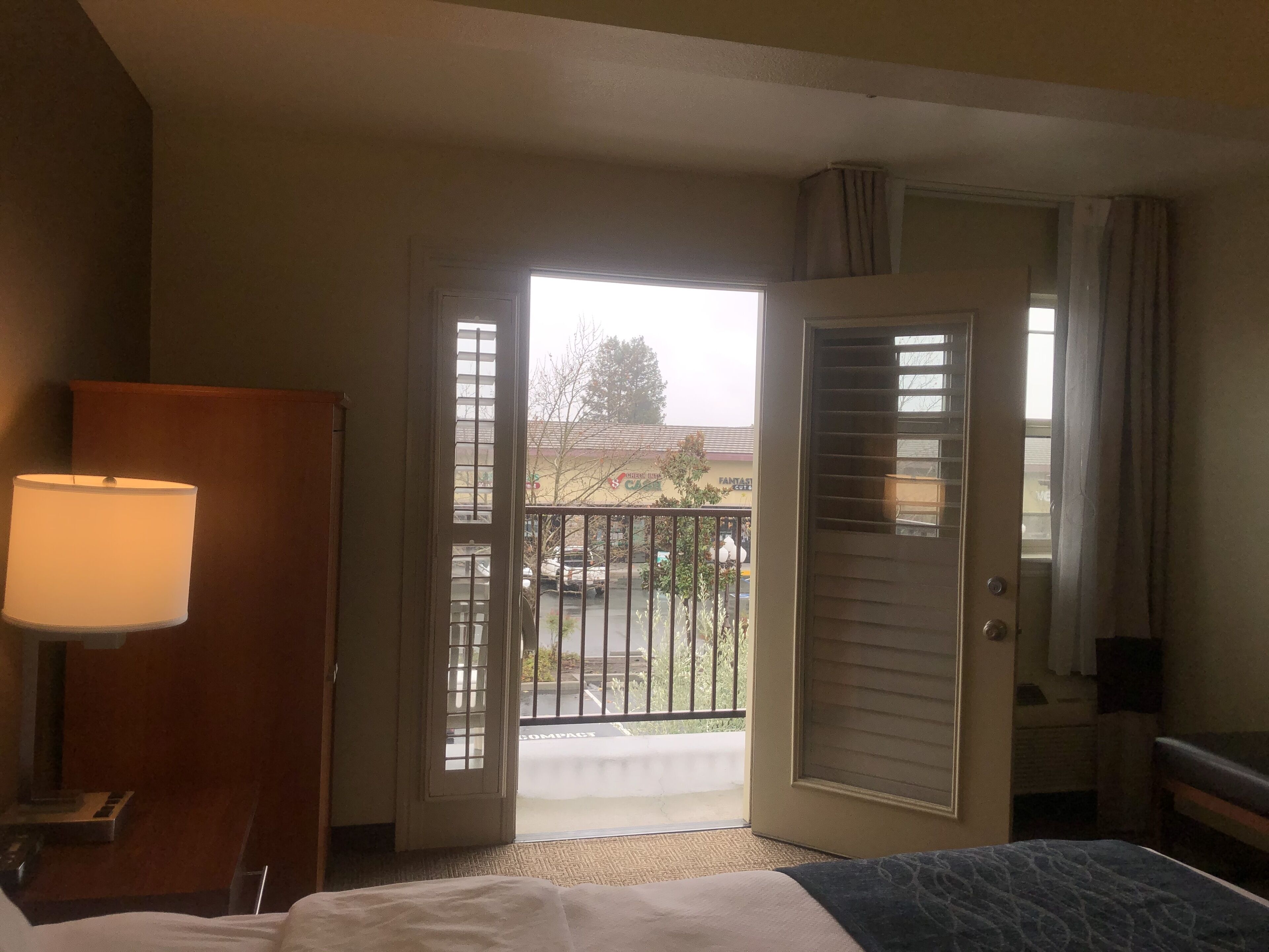 A hotel room with a bed, a desk, a lamp, and a door leading to a balcony.