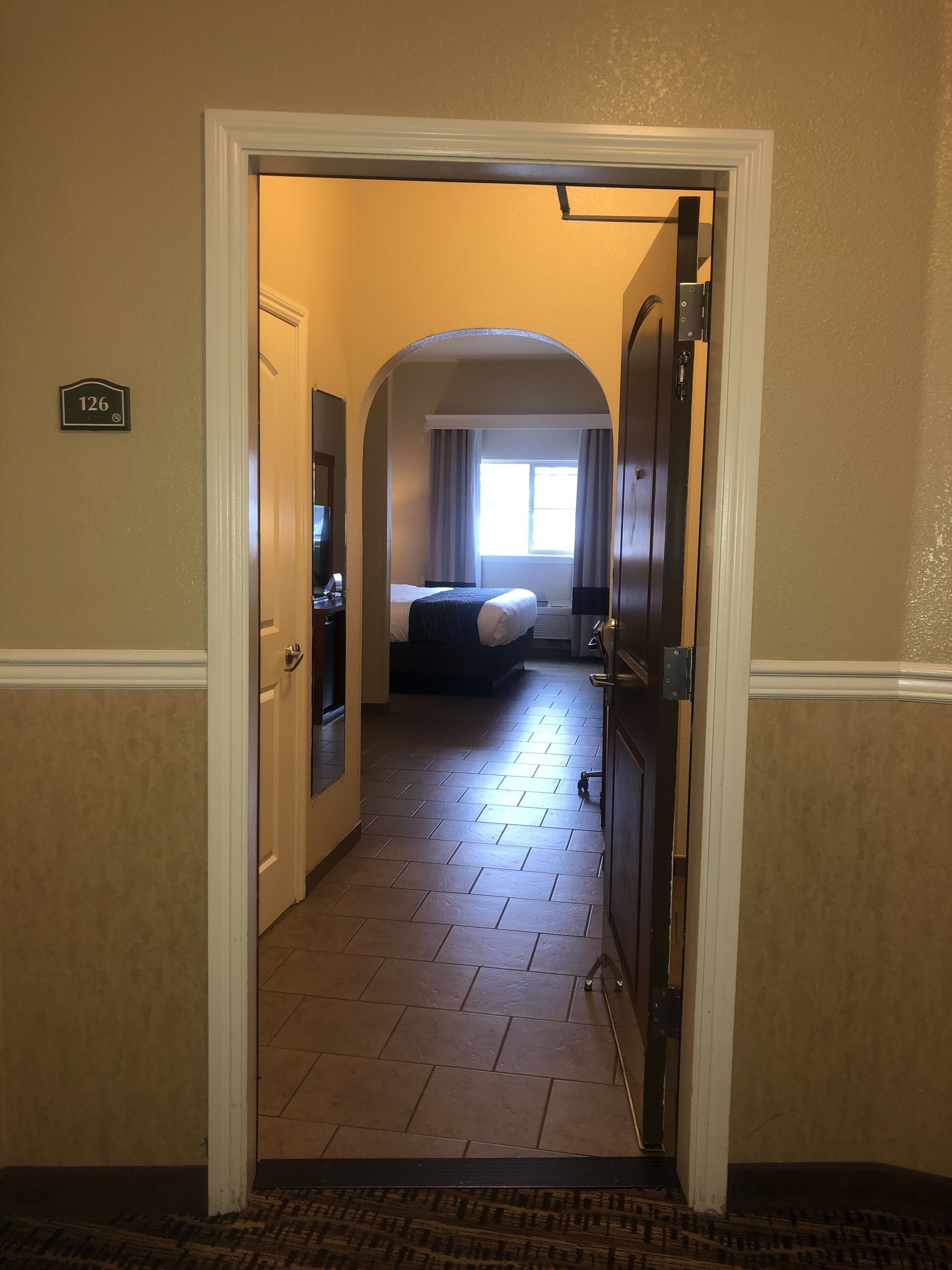 Ein Hotelflur, der zu einem Schlafzimmer mit Bett, Schreibtisch und Fenster führt.