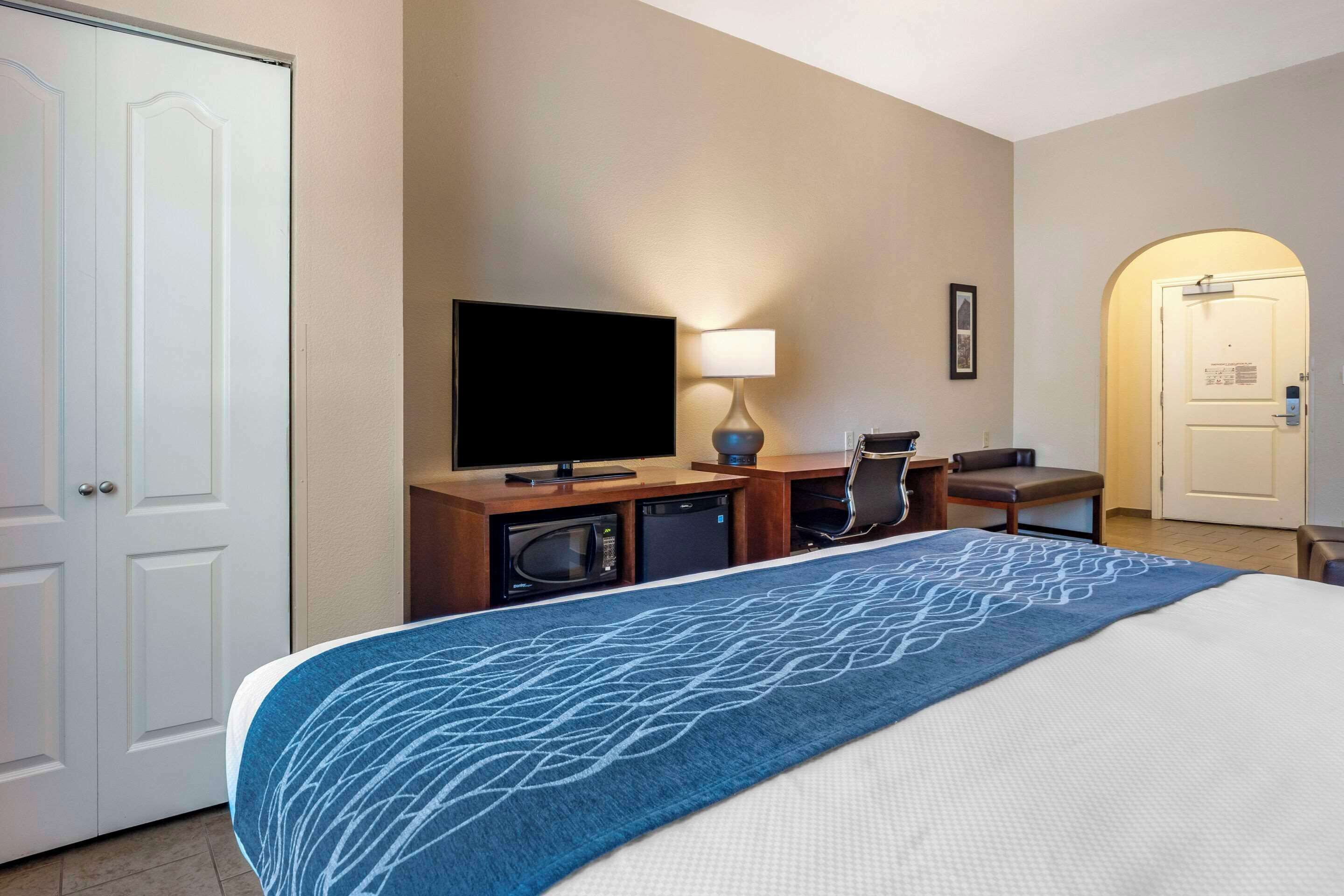 A hotel room with a bed, a TV, a desk with a lamp, a chair, and a microwave.