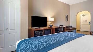 A hotel room with a bed, a TV, a desk with a lamp, a chair, and a microwave.
