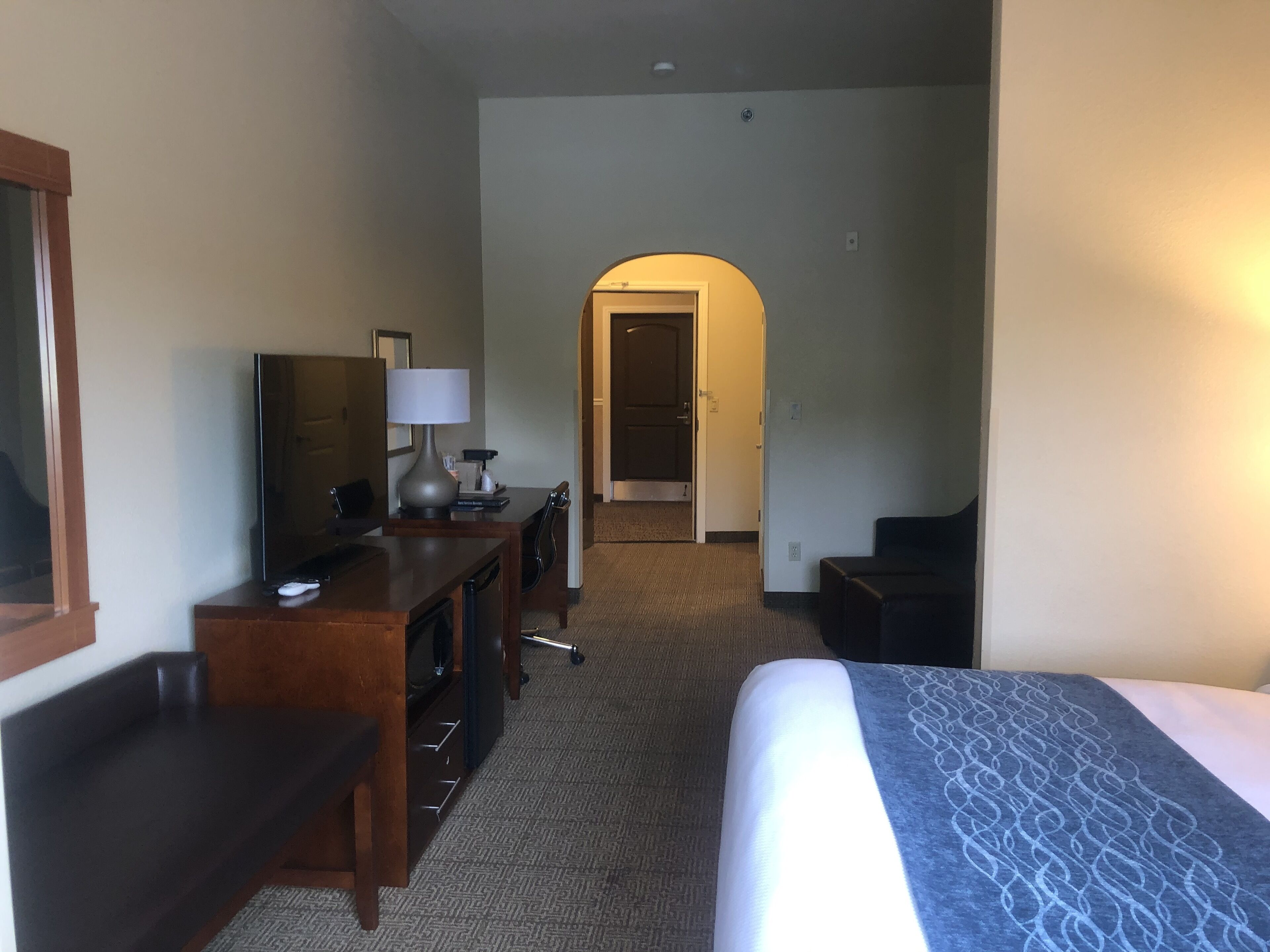 A hotel room with a bed, a desk, a chair, a lamp, and a television.