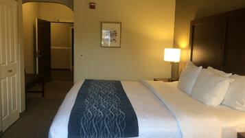 Una habitación de hotel con una cama, una mesita de noche, una lámpara, un cuadro en la pared y una puerta que da a otra habitación.