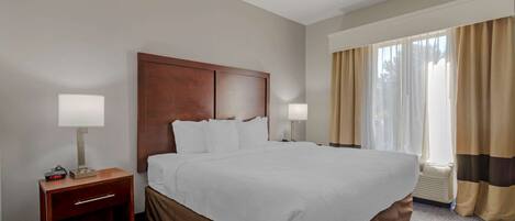 Habitación de hotel con una cama grande, dos lámparas de noche, una mesita de noche y un ventanal con cortinas.