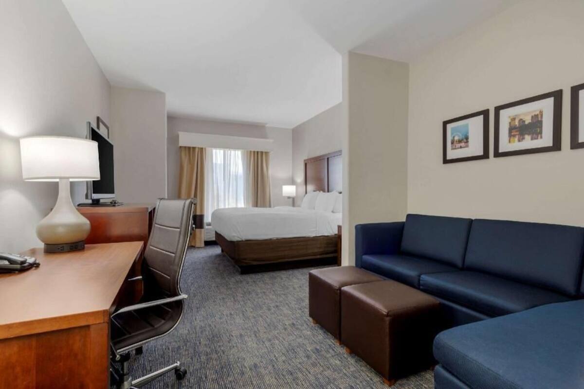 A hotel room with a bed, a desk with a lamp, a sofa, and a TV.