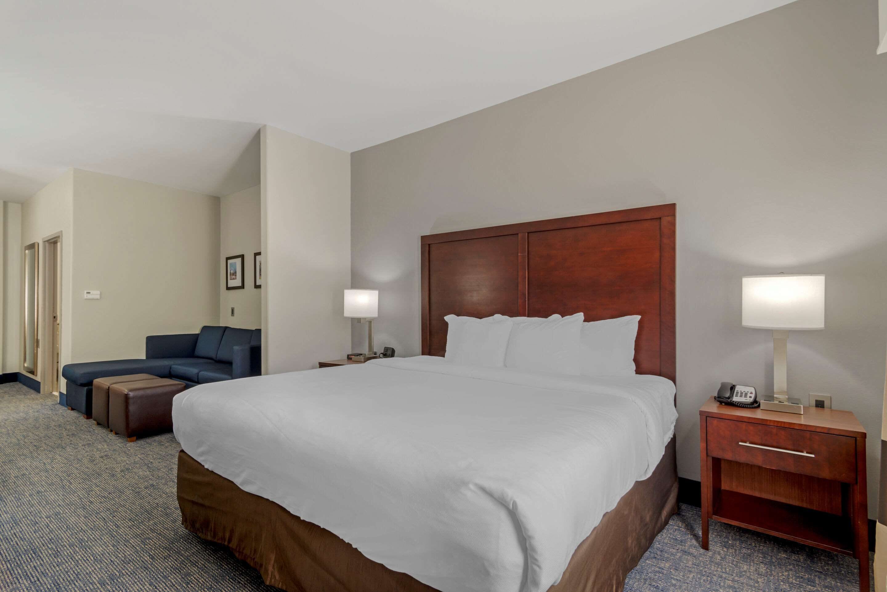 A hotel room with a large bed, a sofa, a nightstand with a lamp, and a desk with a phone.