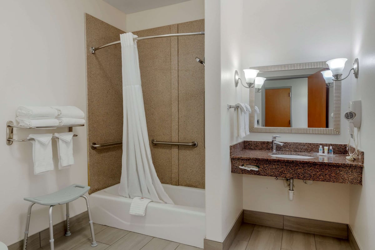 A bathroom with a shower, a grab bar, a step stool, a sink with a mirror, and towels on a rack.