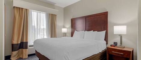 Habitación de hotel con una cama grande, cabecero de madera, dos lámparas de noche, mesita de noche y una ventana con cortinas.