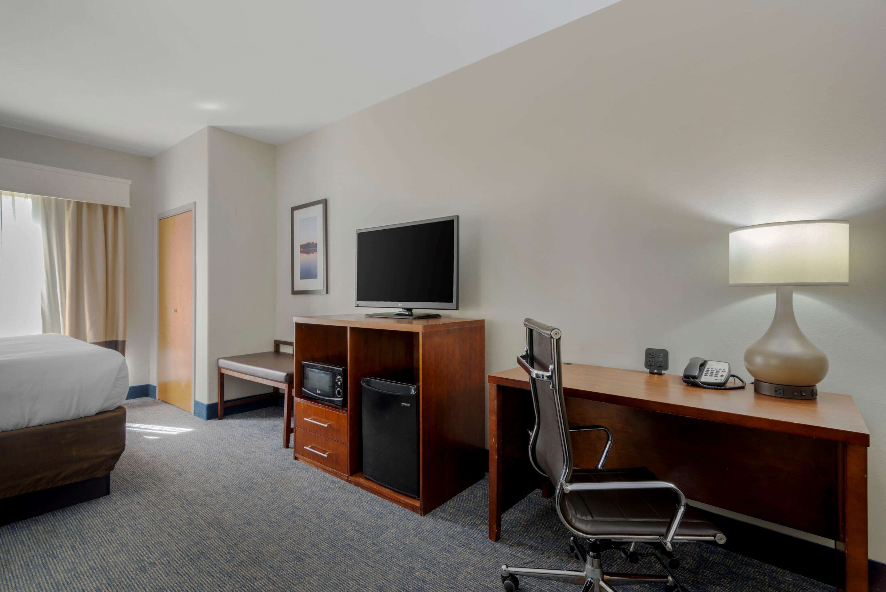 A hotel room with a bed, a desk with a computer, a television, a lamp, and a telephone.