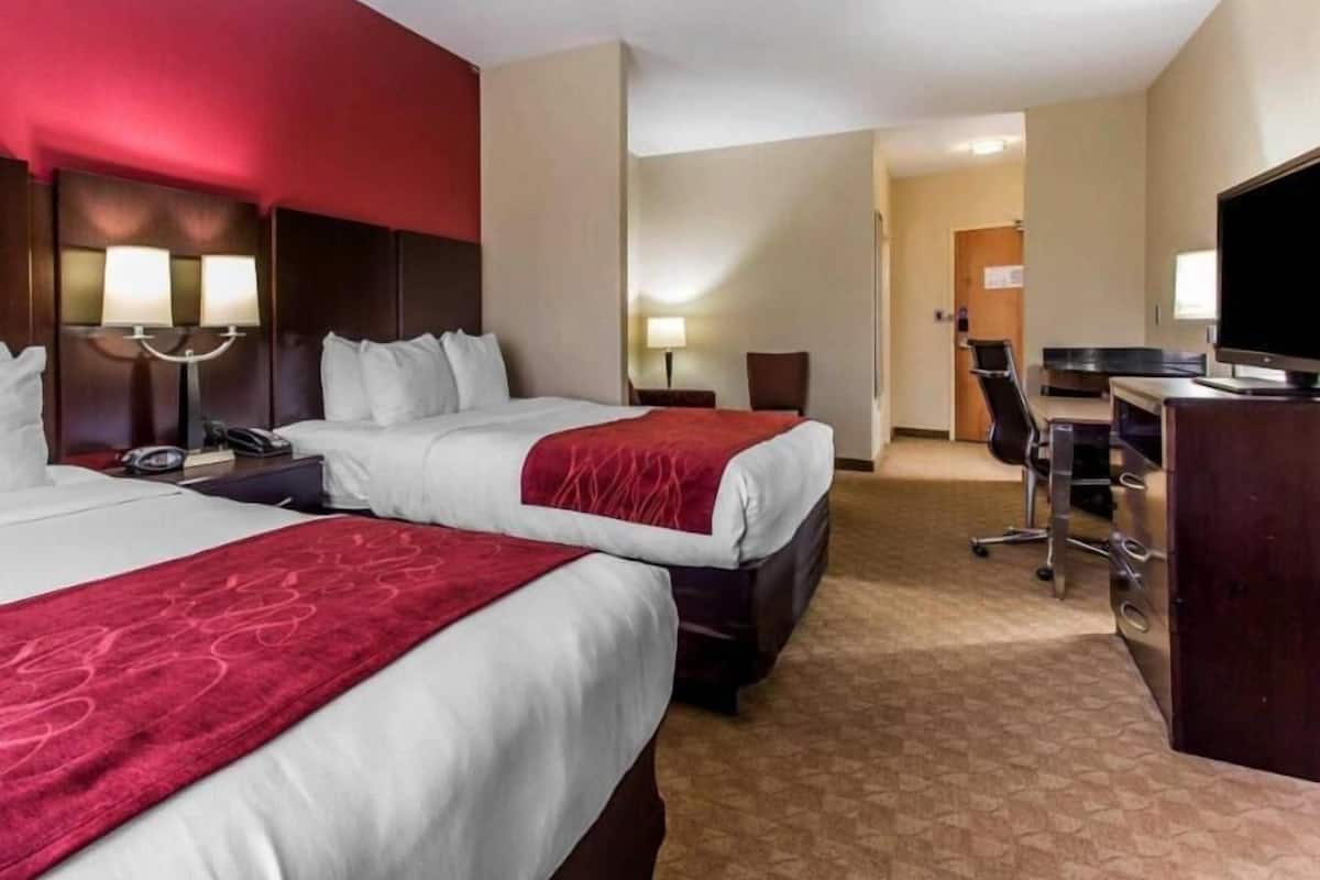 A hotel room with two beds, a desk, a TV, and a door leading to a hallway.