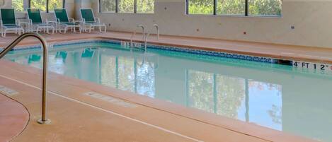 Una piscina interior con agua cristalina, un trampolín y sillones de descanso.