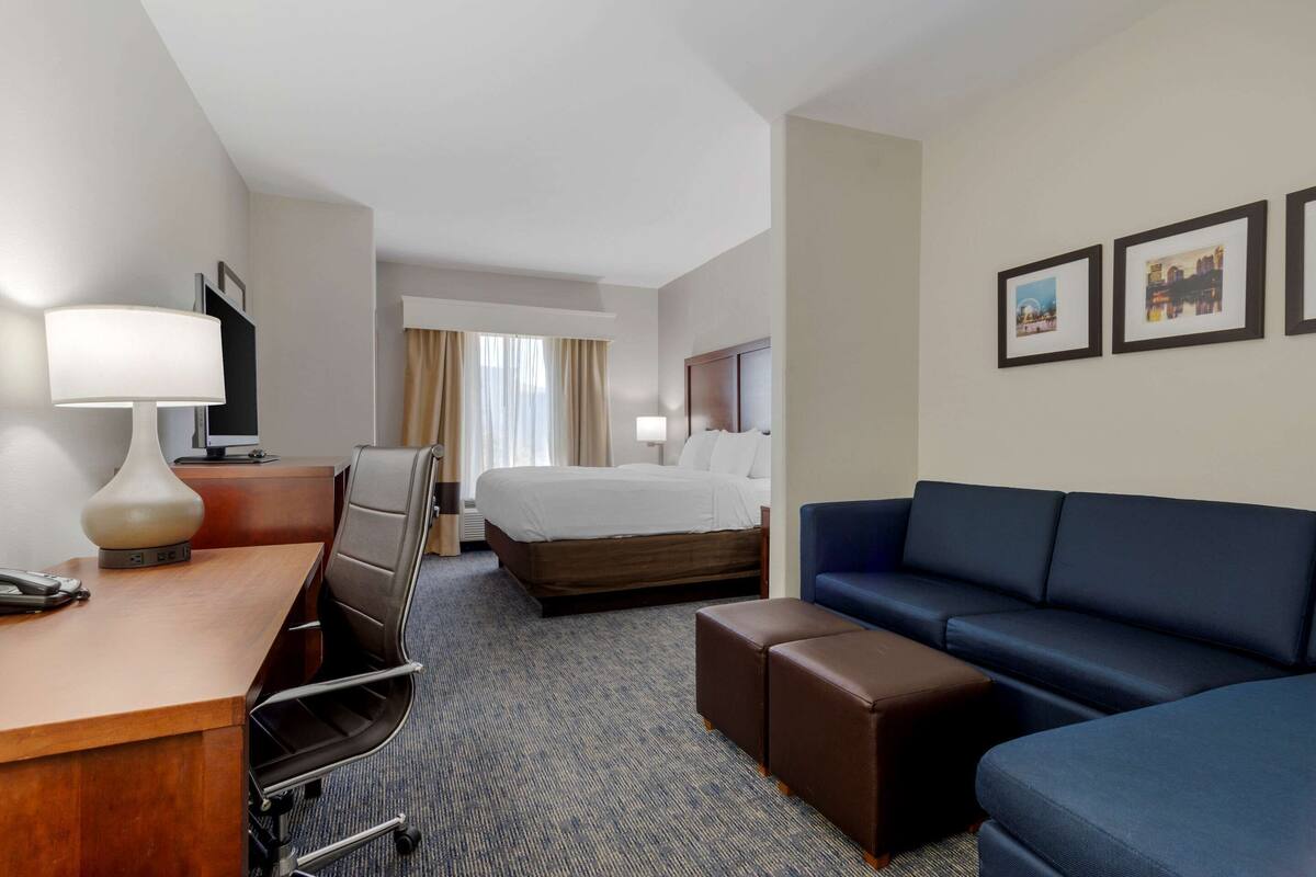 A hotel room with a bed, a desk with a lamp, a blue sofa, and a small table.