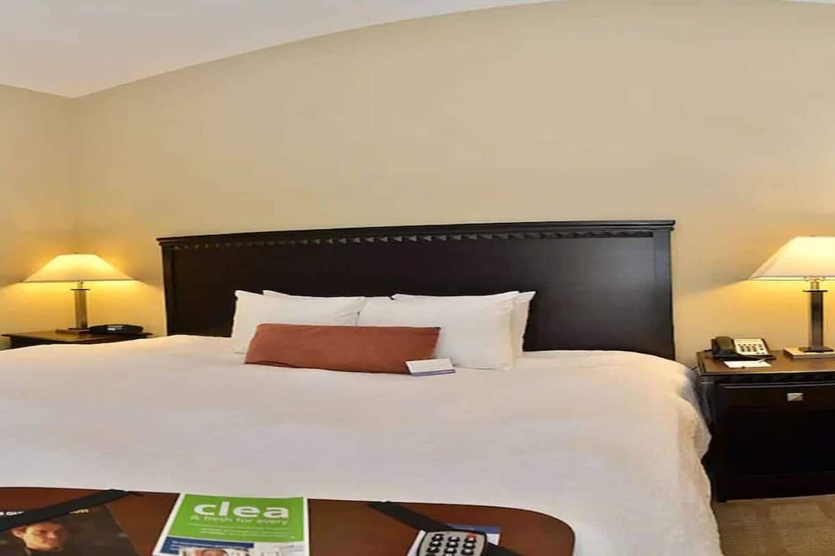 A hotel room with a large bed, two bedside tables with lamps, a desk with a telephone, and a refrigerator.