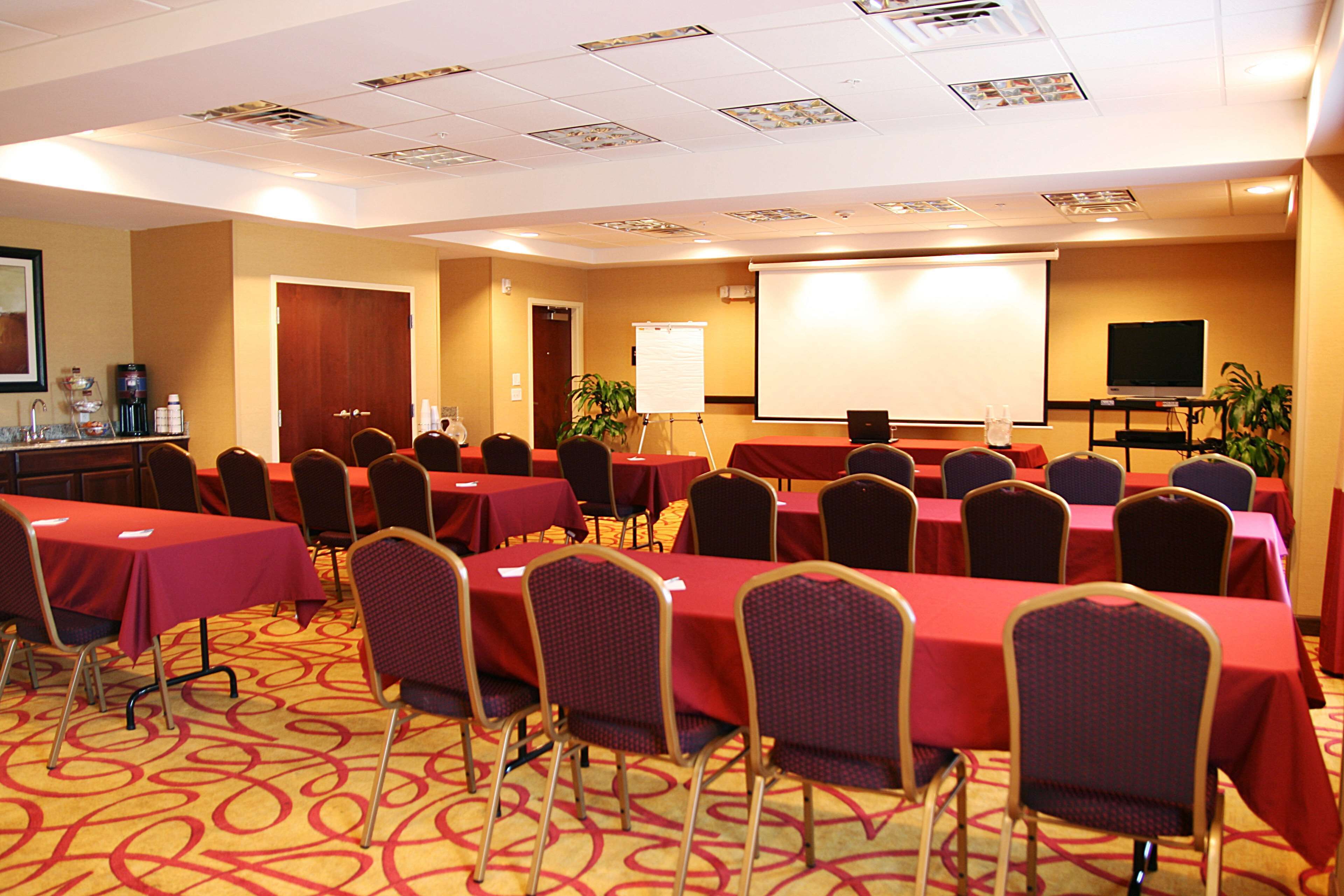 A conference room with multiple tables and chairs, a projector screen, and a water cooler.