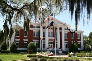 A large, stately building with a red brick facade, white columns, and a flagpole with an American flag. - Hampton Inn Dade City - Zephyrhills (Dade City)