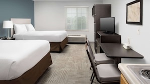Hotelkamer met twee bedden, een bureau, een stoel, een televisie, een verwarming en een raam met zonwering.