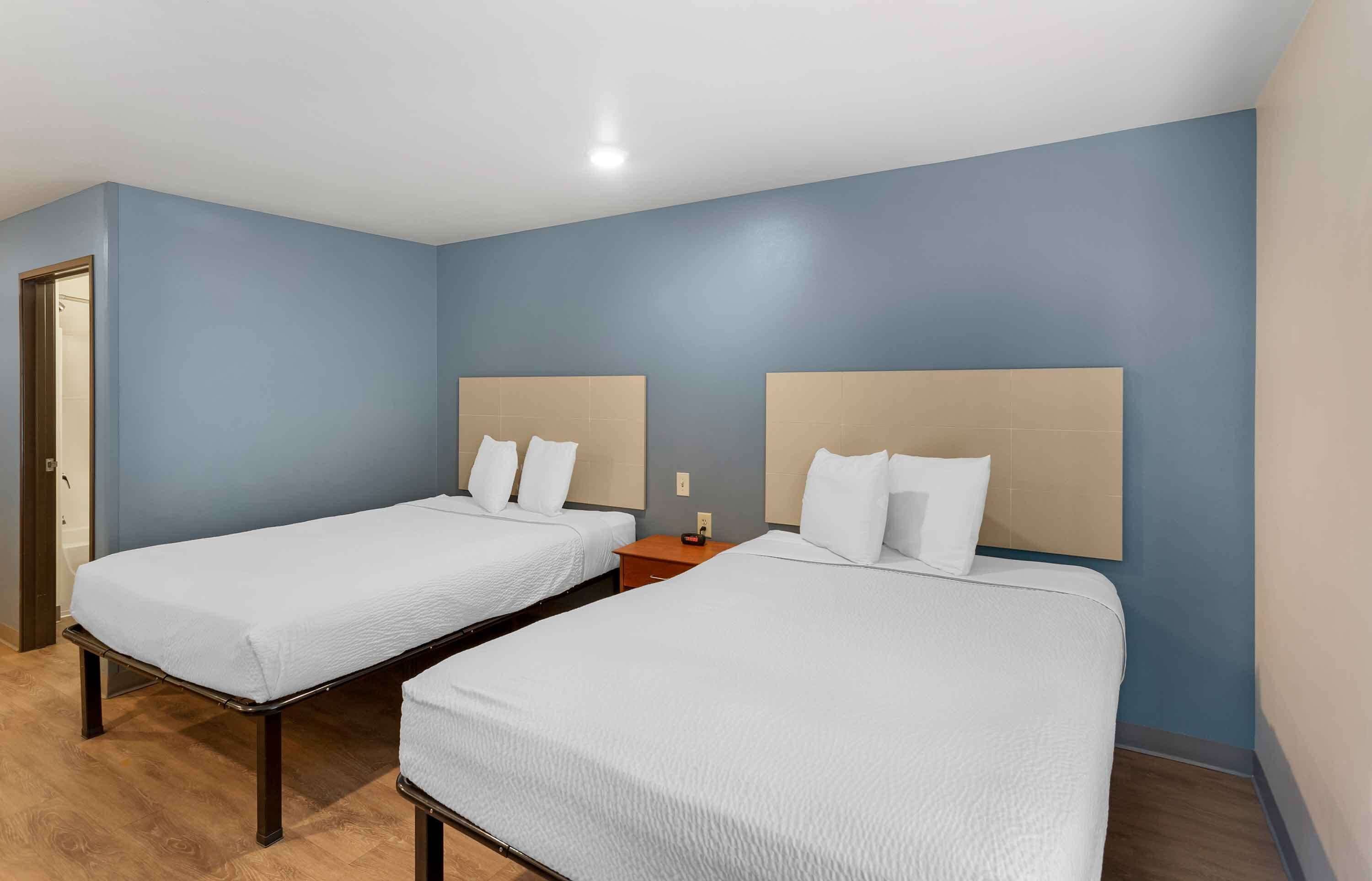 A hotel room with two single beds, wooden flooring, and light blue walls.