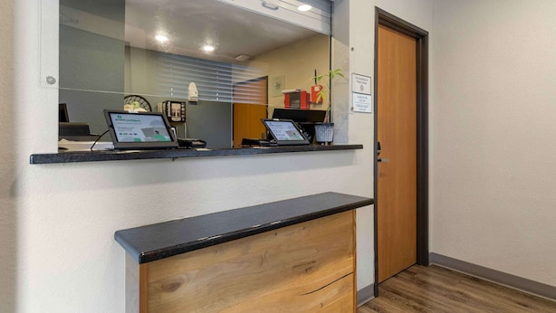 A reception desk with a computer, a wooden cabinet, and a door. - Extended Stay America Select Suites - Austin - Round Rock (Round Rock)