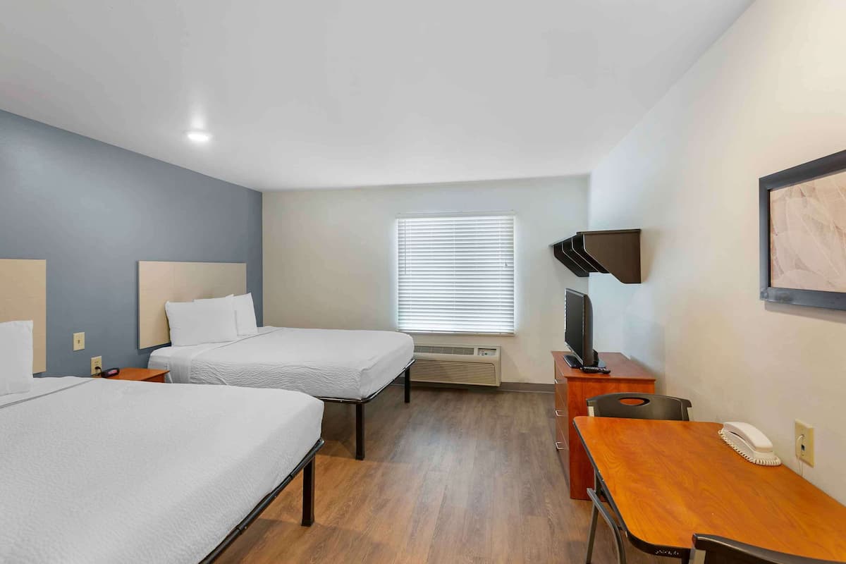 A hotel room with two beds, a desk, a chair, a television, and a window with blinds.