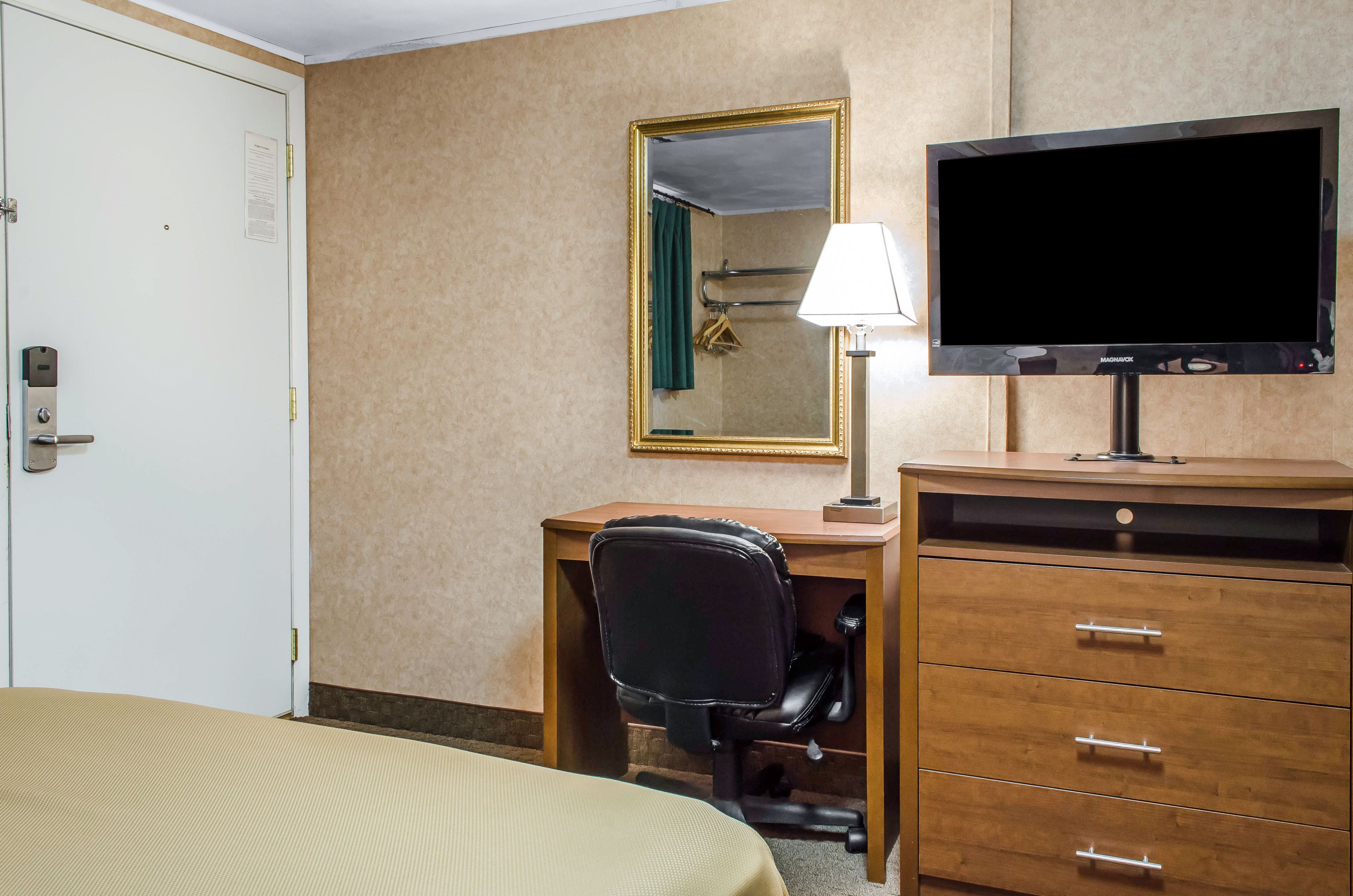 Une chambre d’hôtel comprenant un lit, un bureau avec une chaise, une télévision, un miroir et une commode.
