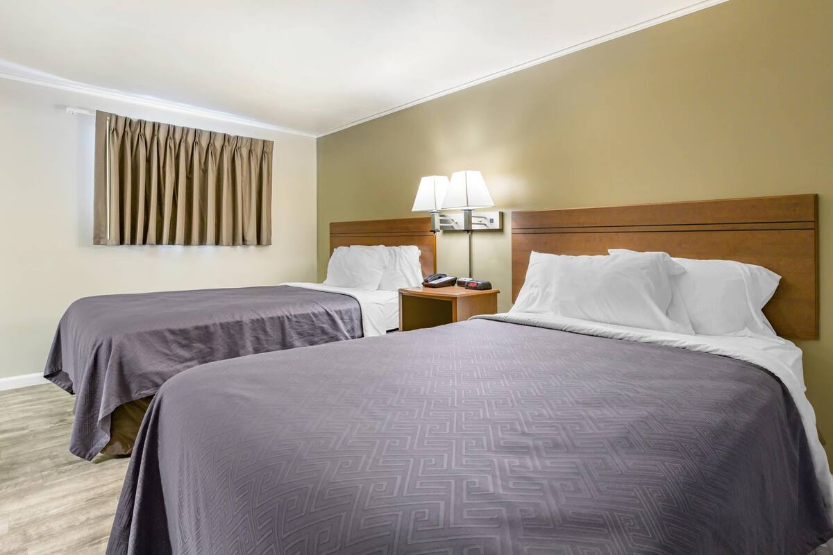 A hotel room with two beds, a nightstand with a lamp, and a window with curtains.