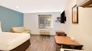 A hotel room with a bed, a desk, a chair, a TV, and a window with blinds. - WoodSpring Suites Charlotte Shelby (Shelby)