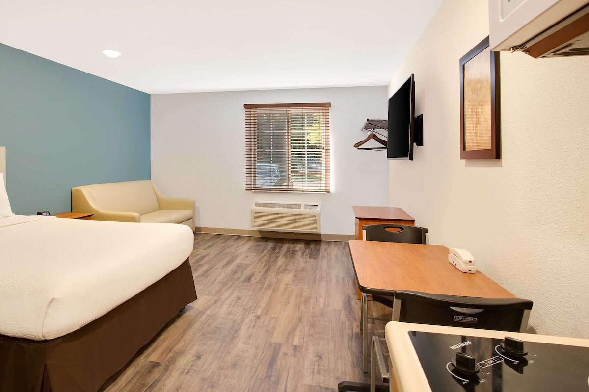 Une chambre d’hôtel équipée d’un lit, d’un bureau, d’une chaise, d’une télévision et d’une fenêtre avec des stores.