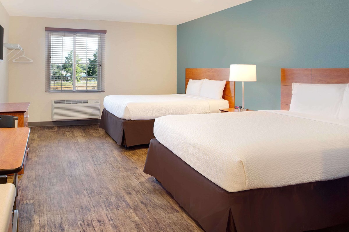 Une chambre d’hôtel avec deux lits, un bureau et une fenêtre avec des stores.