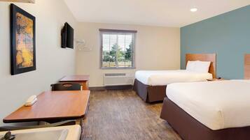 A hotel room with two beds, a desk, a chair, a TV, a window with blinds, and a radiator.
