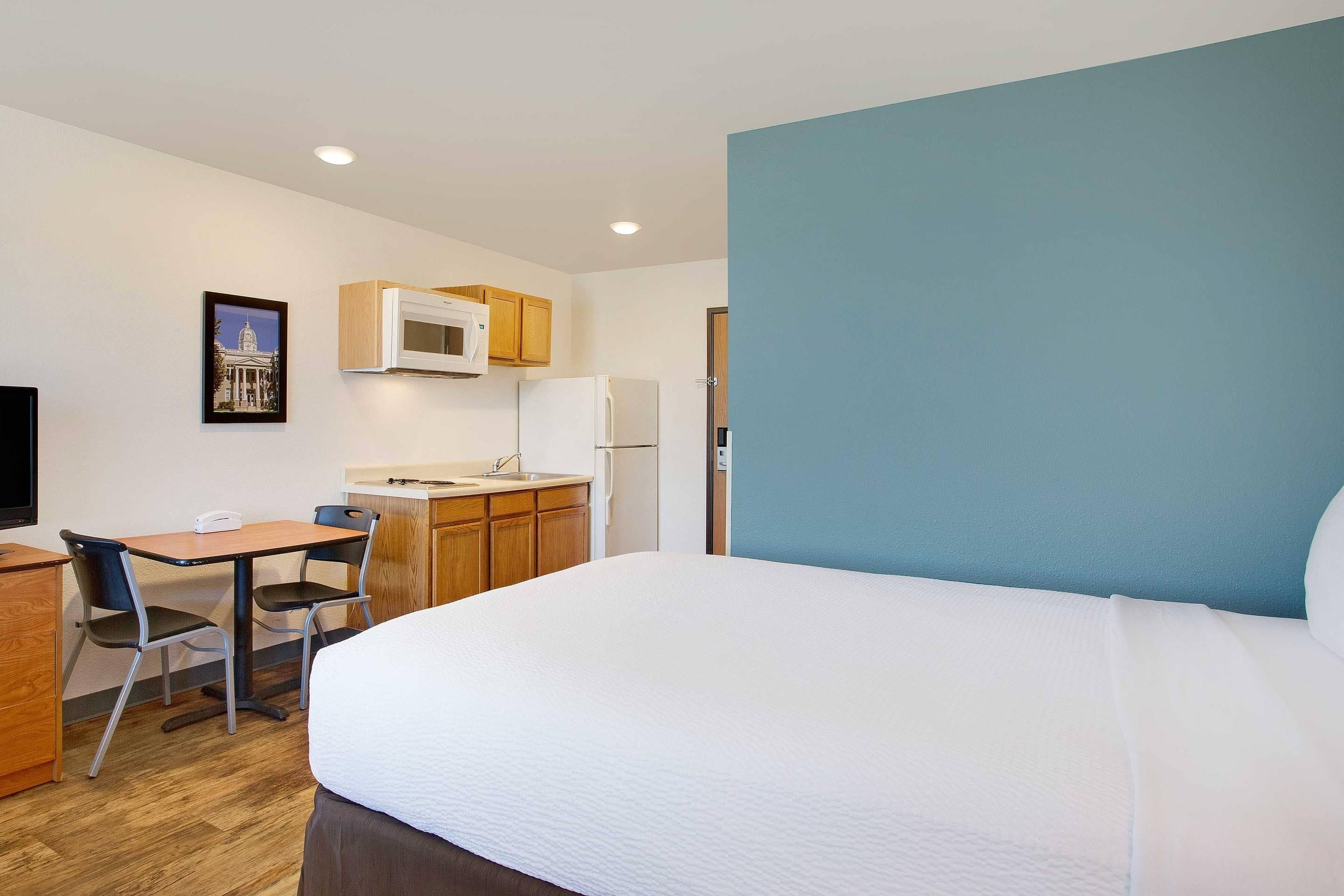 A hotel room with a bed, a desk with a chair, a microwave, a refrigerator, and a sink.