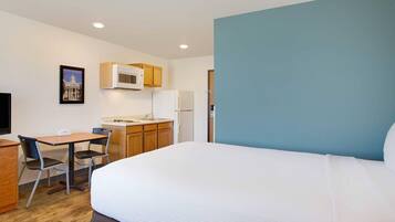 Habitación de hotel con cama, escritorio con silla, microondas, refrigerador y lavamanos.