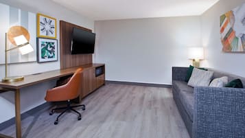 A modern hotel room with a wooden desk, a comfortable sofa, a flat-screen TV, and artwork on the walls.