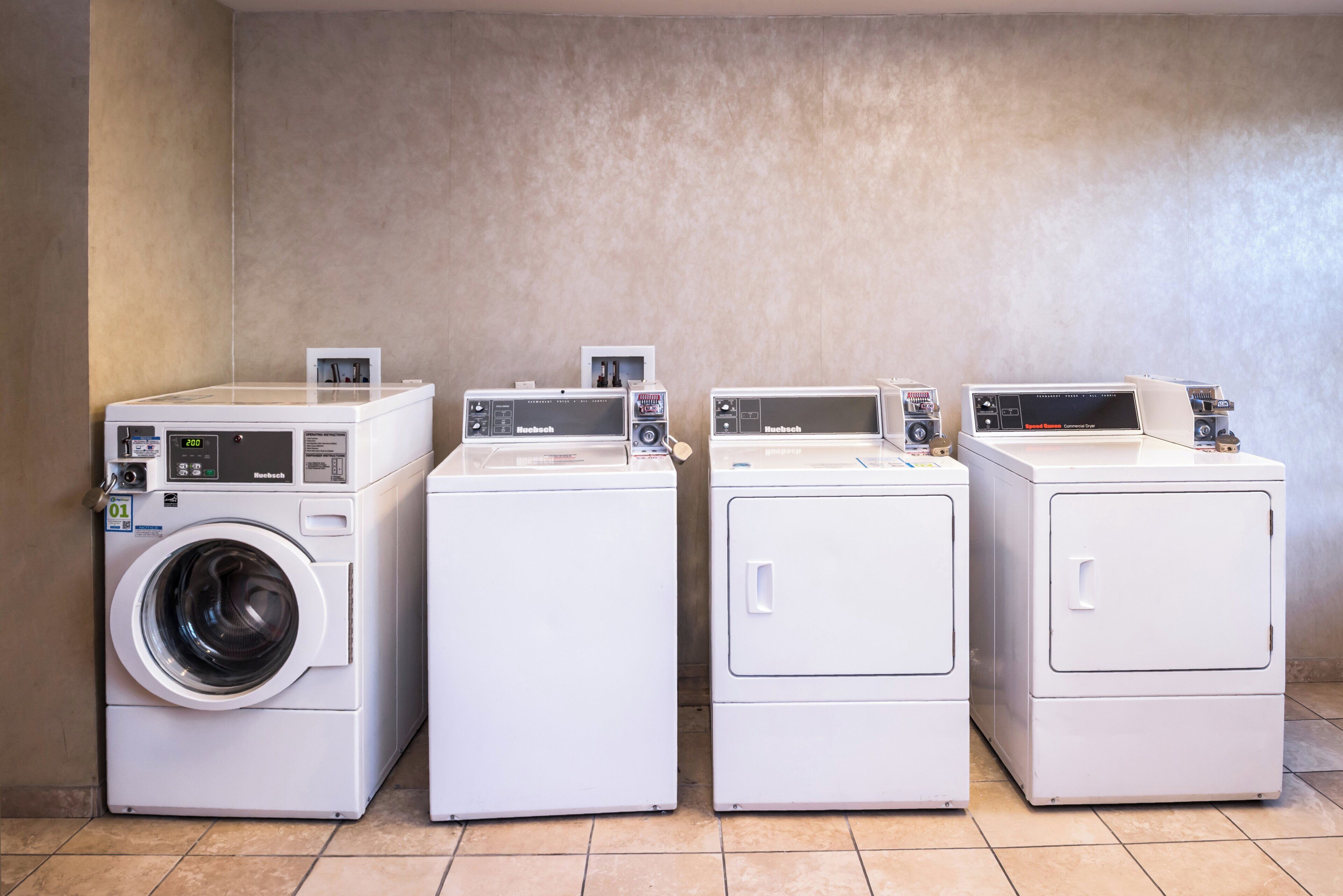 Four white front-loading washing machines in a row against a plain wall.