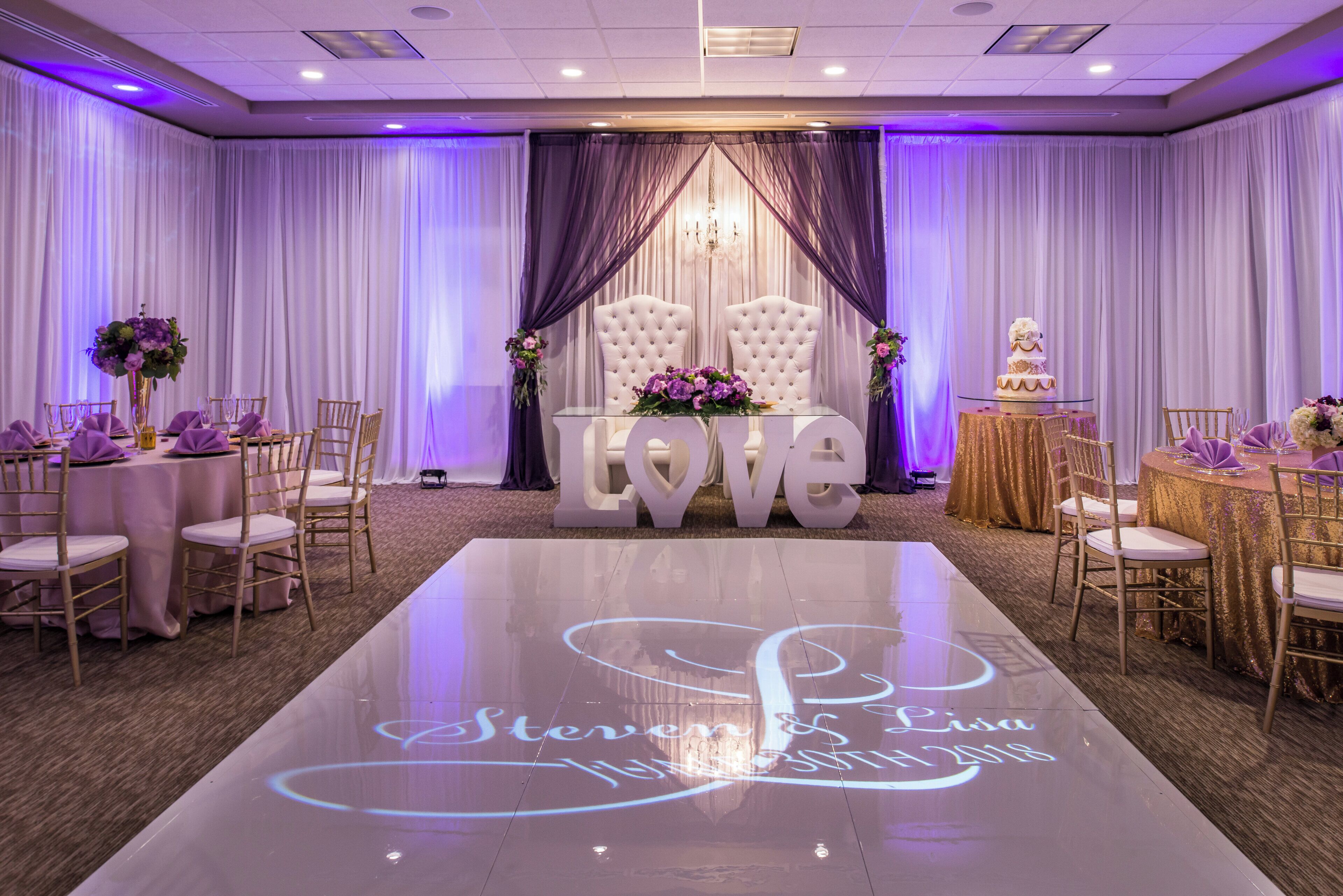 A wedding reception area with a dance floor, tables, chairs, and a stage with a 'LOVE' backdrop.