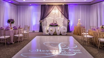 A wedding reception area with a dance floor, tables, chairs, and a stage with a 'LOVE' backdrop.
