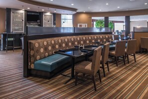 A restaurant with a booth seating area, a bar, and a dining area with chairs and tables. - Holiday Inn Ontario Airport by IHG (Ontario)