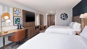 A hotel room with two beds, a desk, a chair, a TV, and artwork on the walls.